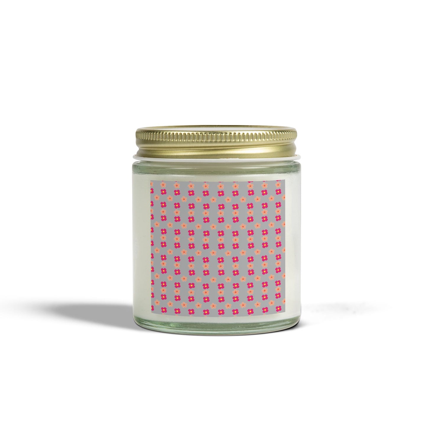 A scented candle with a gold lid and a label featuring a pink geometric pattern, placed against a plain background.