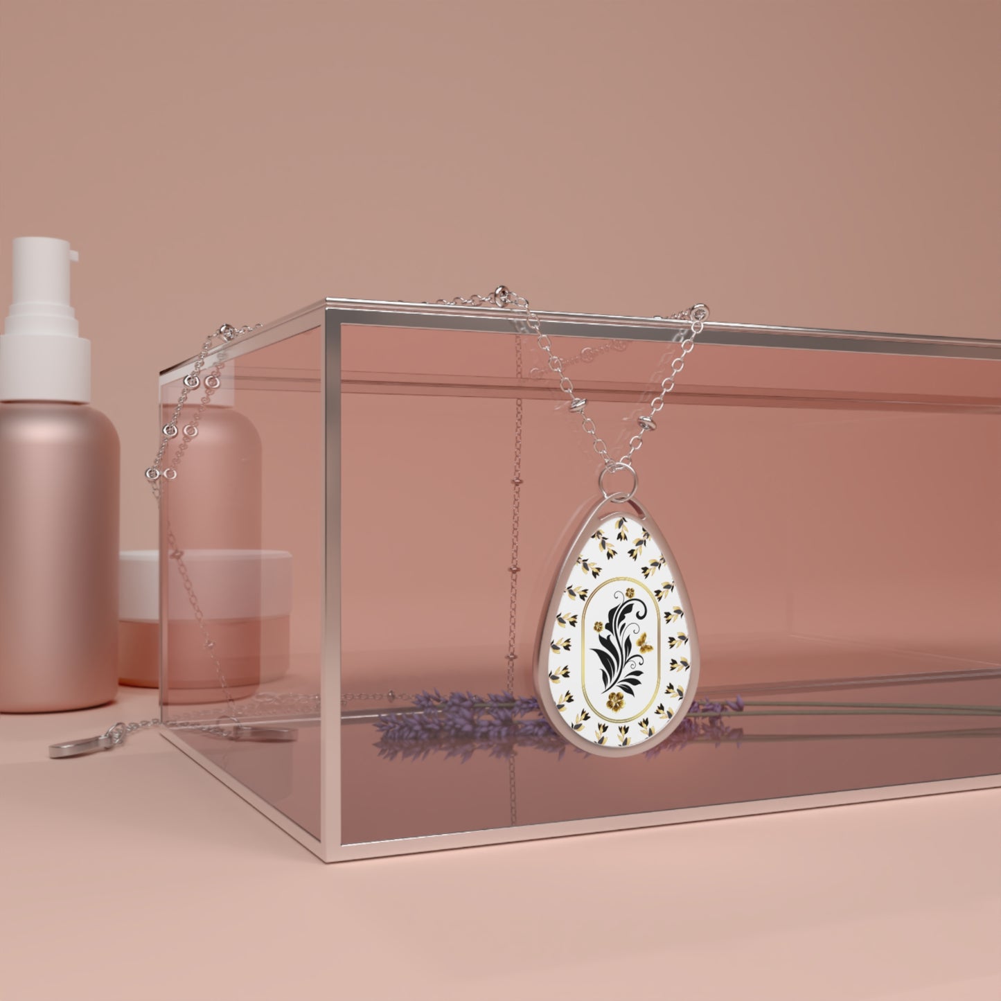 Teardrop-shaped pendant with floral design on a chain, placed inside a clear box with a pink background.