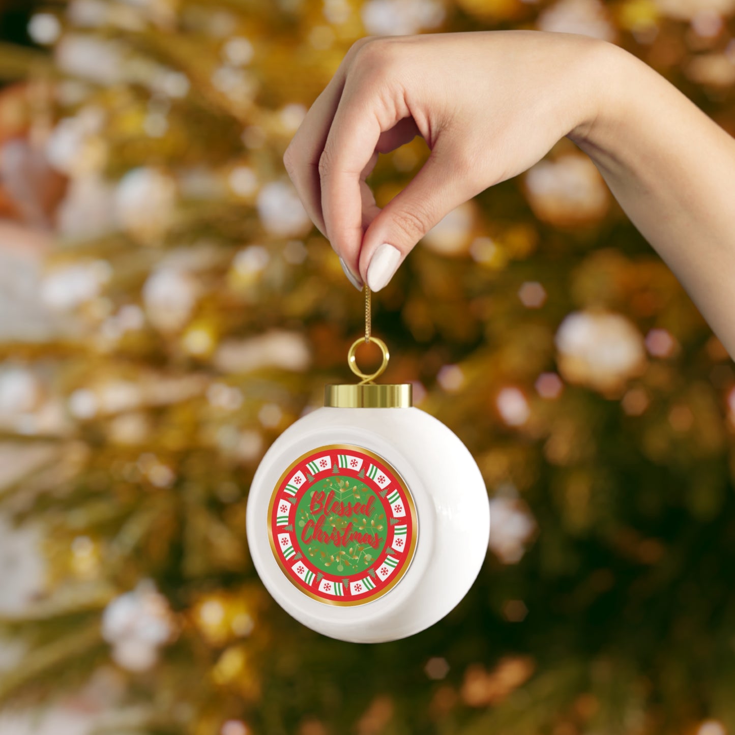 Hand holding a Christmas ornament with a festive design against a blurred Christmas tree background