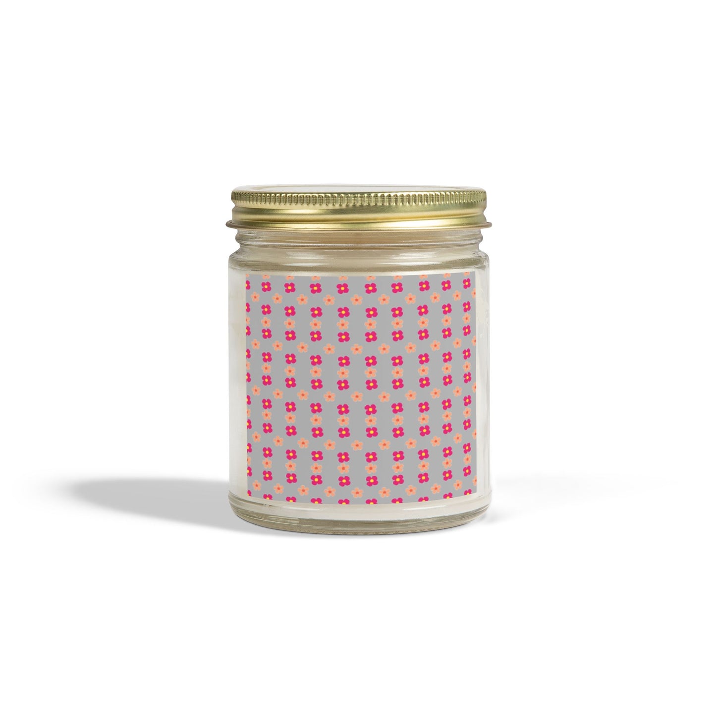 A scented candle with a gold lid and a label featuring a pink geometric pattern, placed against a plain background.