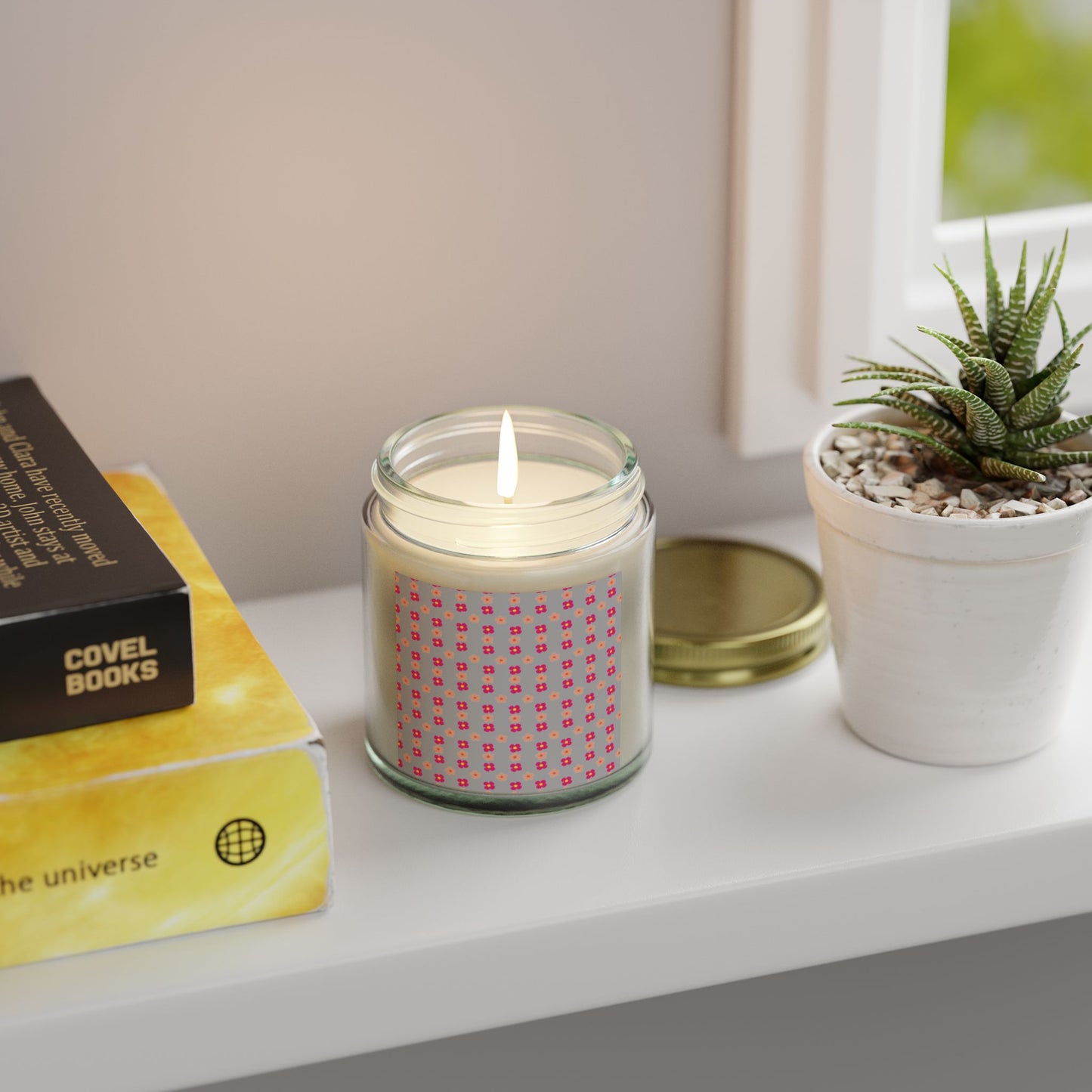 Candle in a glass jar on a shelf with a book and plant.