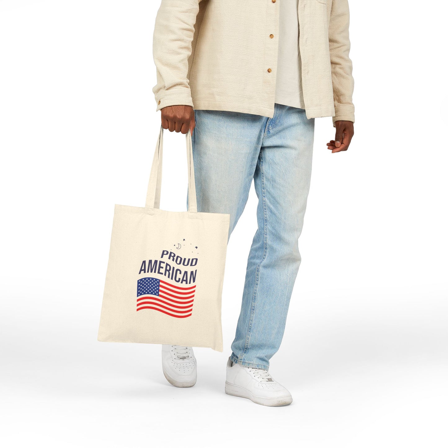 Person holding a tote bag with 'Proud American' text and flag design on a white background