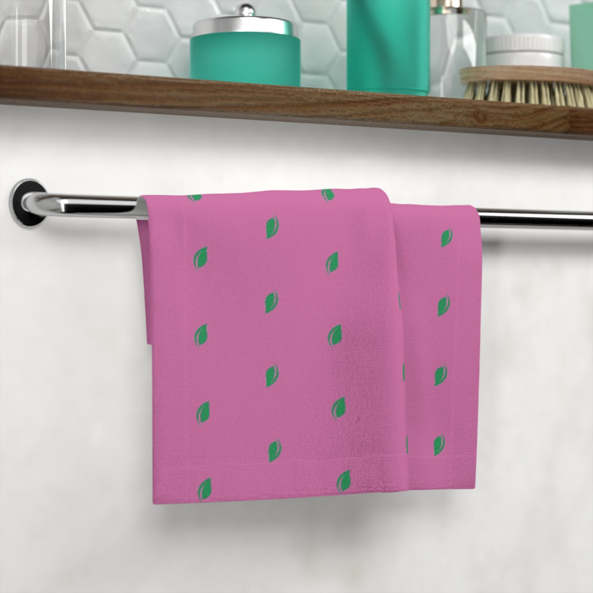 Pink towel with green leaf patterns hanging on a towel rack in a bathroom.