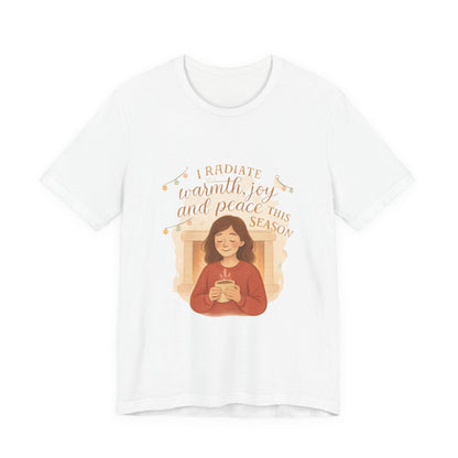 White t-shirt with a graphic of a person holding a mug and text 'I radiate warmth, joy, and peace this season' on a white background.