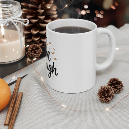 White mug with text, candle, cinnamon sticks, and pine cones on a table.