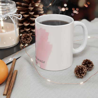 White mug with pink design on a table with candles, oranges, and pinecones.