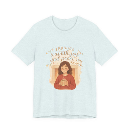 Light blue t-shirt with a graphic of a person holding a mug and text 'I radiate warmth, joy, and peace this season' on a white background.