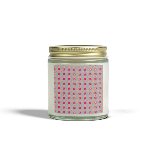A scented candle with a gold lid and a label featuring a pink geometric pattern, placed against a plain background.