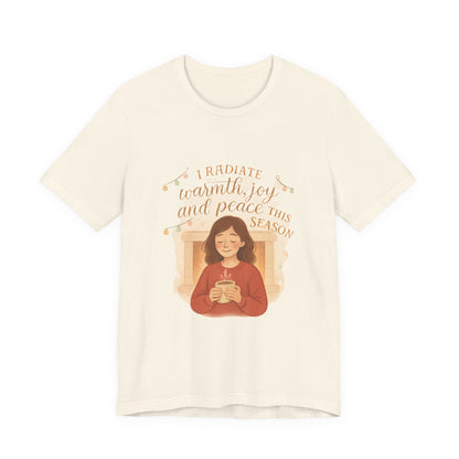 Beige t-shirt with a graphic of a person holding a mug and text 'I radiate warmth, joy, and peace this season' on a white background.