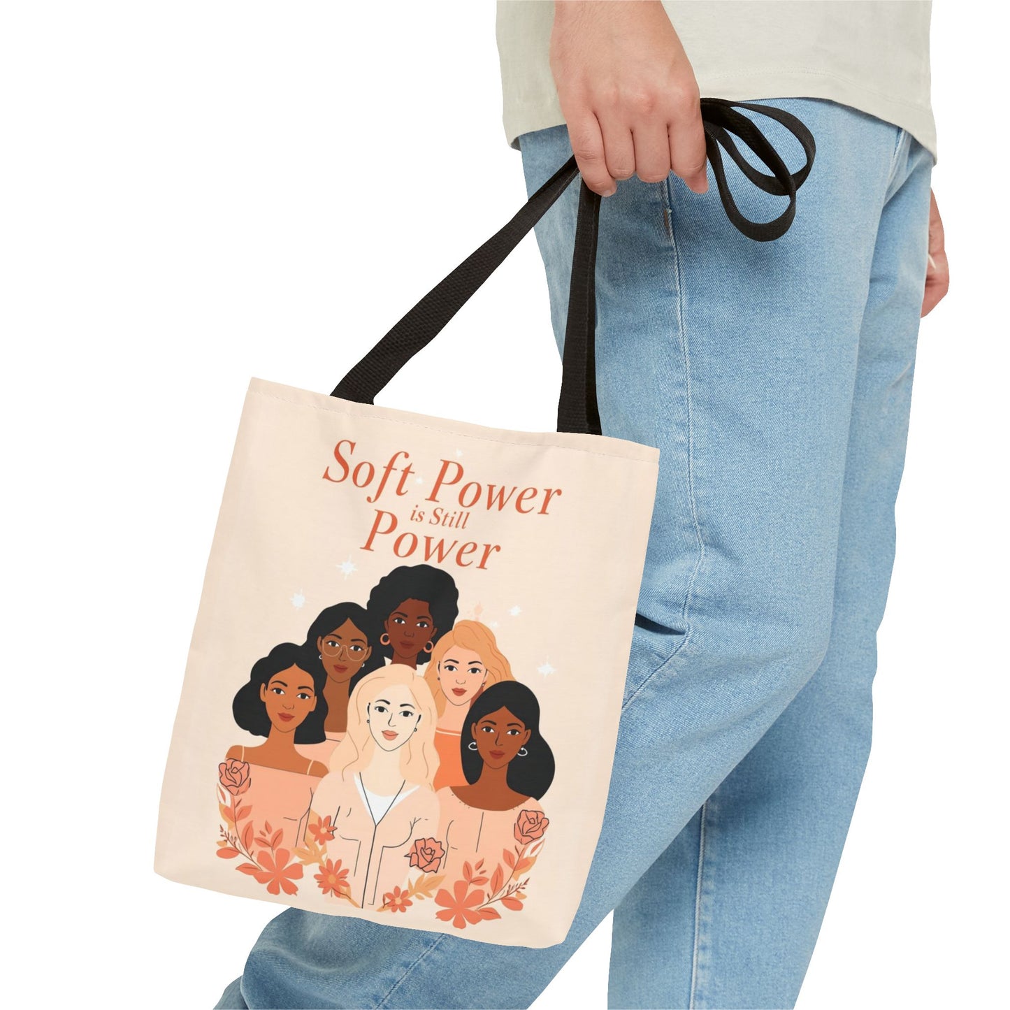 Tote bag with illustrations of diverse women and text 'Soft Power is Still Power' held by a person wearing jeans.