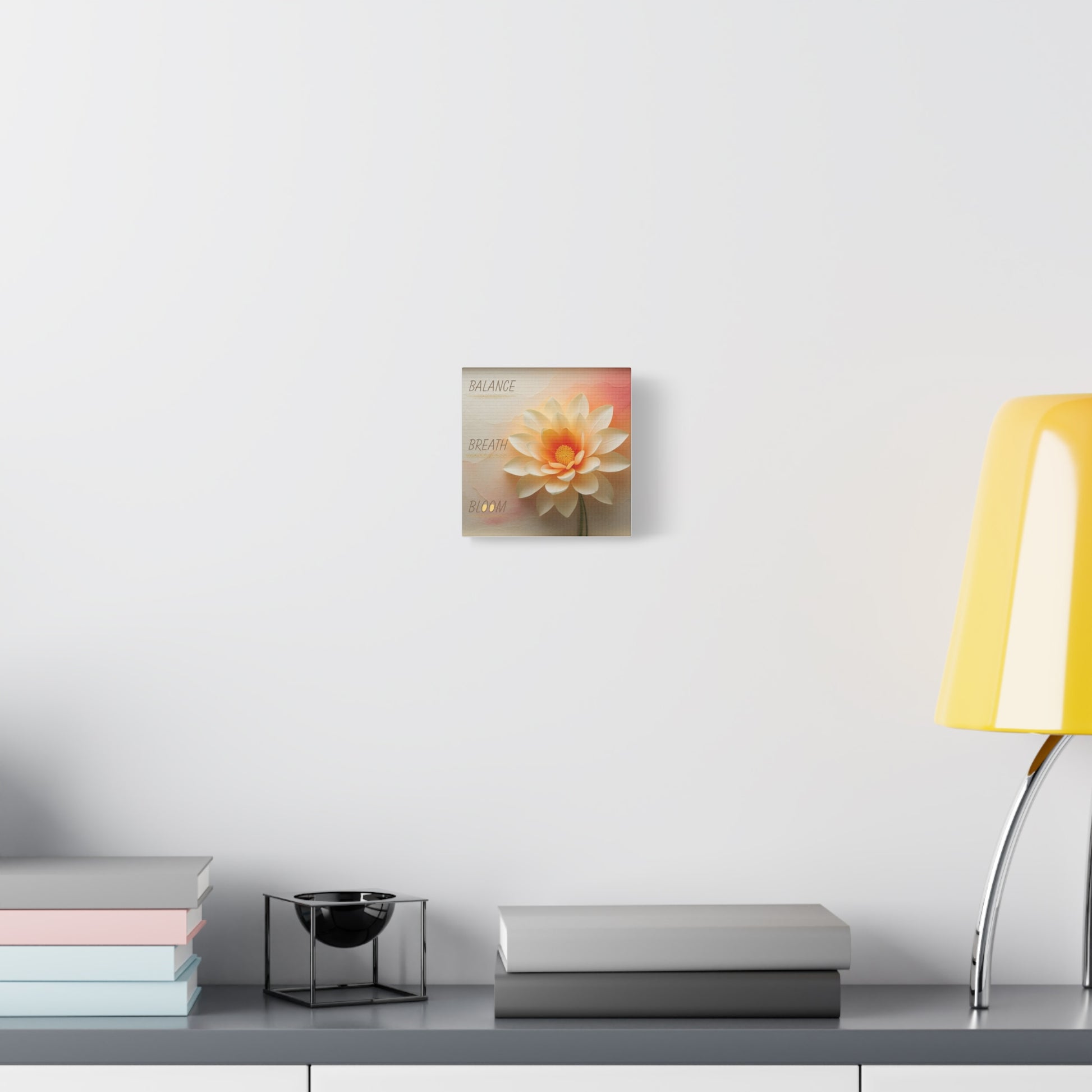 Decorative wall art of a flower on a white wall above a table with a lamp and books.