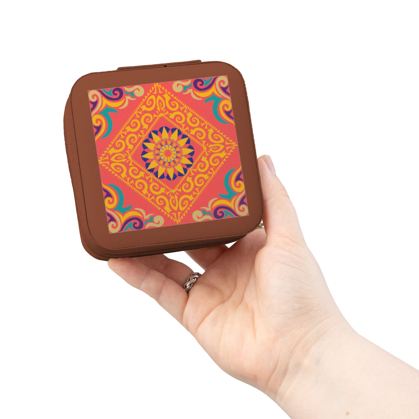 Hand holding a small square travel jewelry case with a colorful pattern on a white background