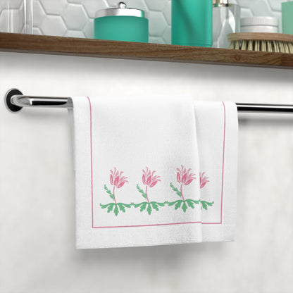 White towel with pink floral design hanging on a towel rack in a bathroom.