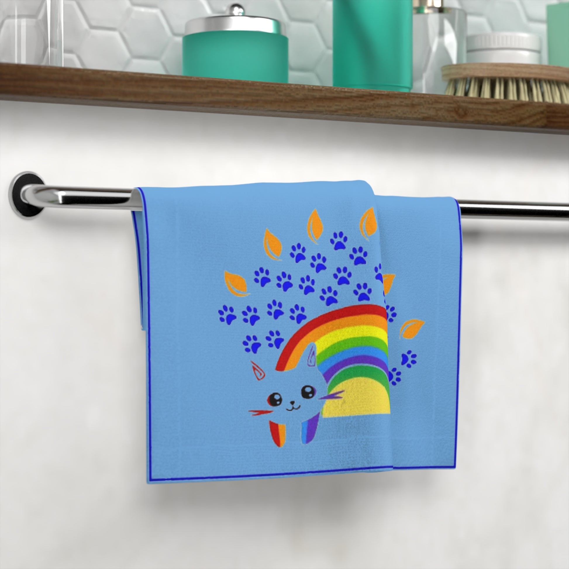 Blue towel with a colorful rainbow and cat design hanging on a towel rack.