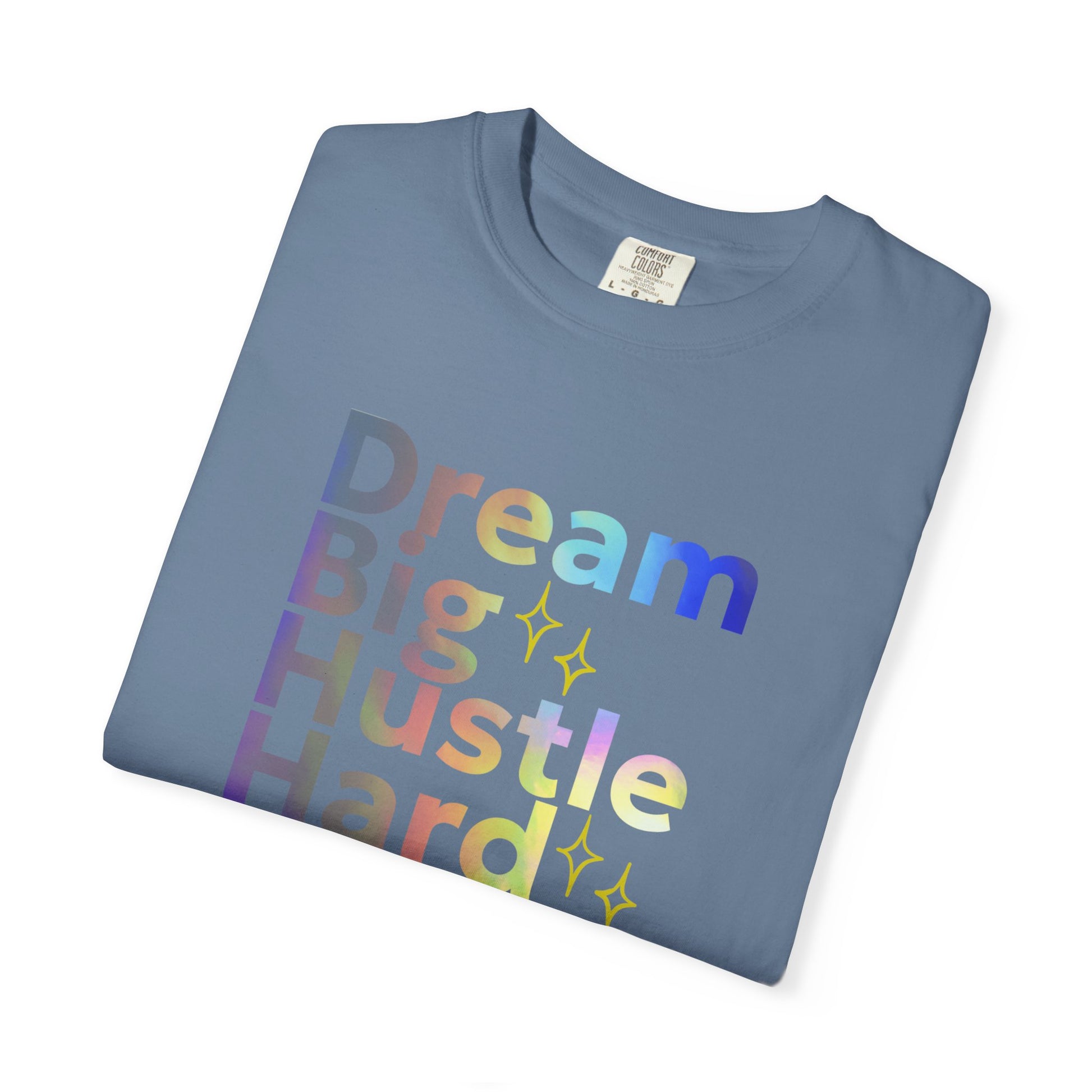 Folded blue t-shirt with motivational text 'Dream Big Hustle Hard' in colorful letters on a white background