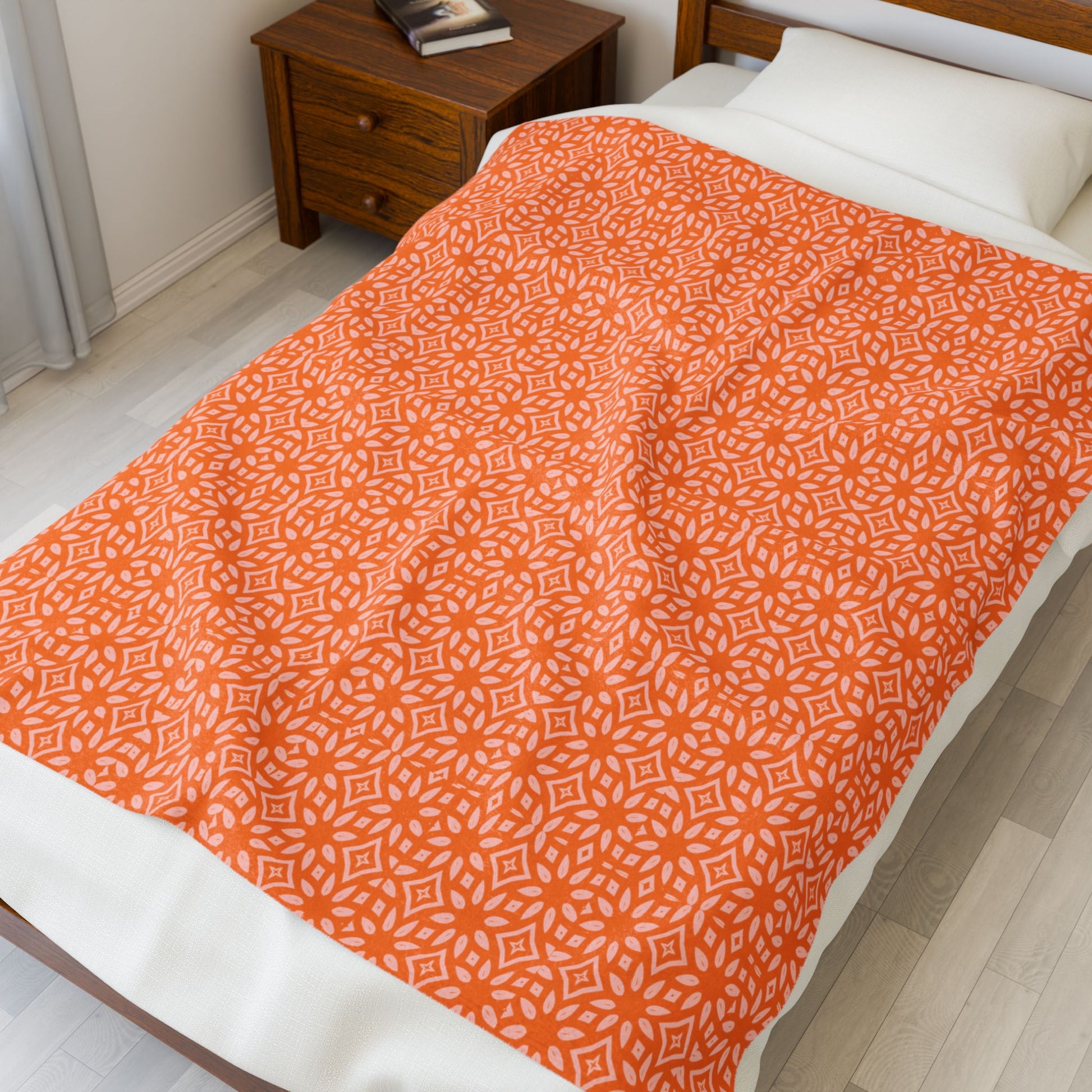 Bed with orange patterned blanket and white pillows in a bedroom setting.