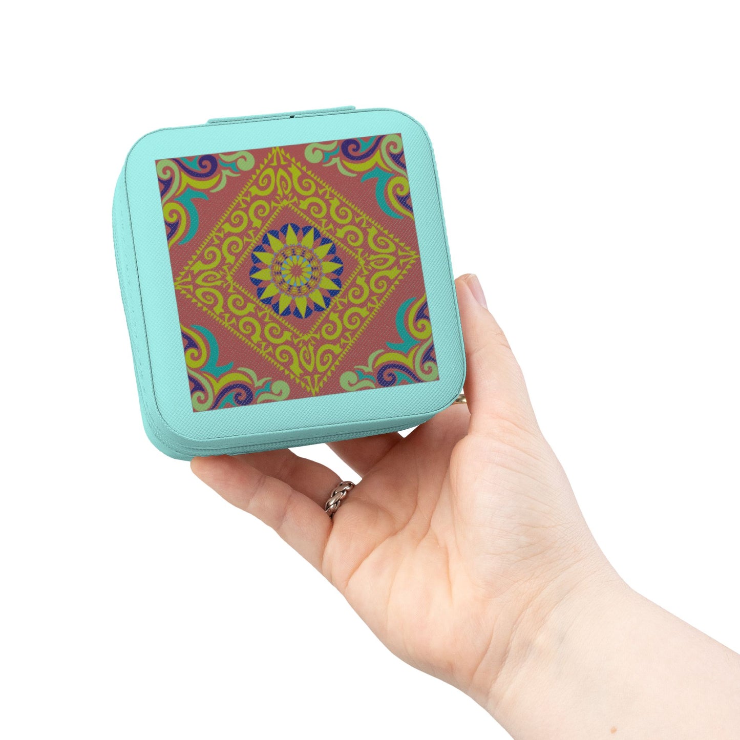 Hand holding a small square travel jewelry case with a colorful pattern on a white background