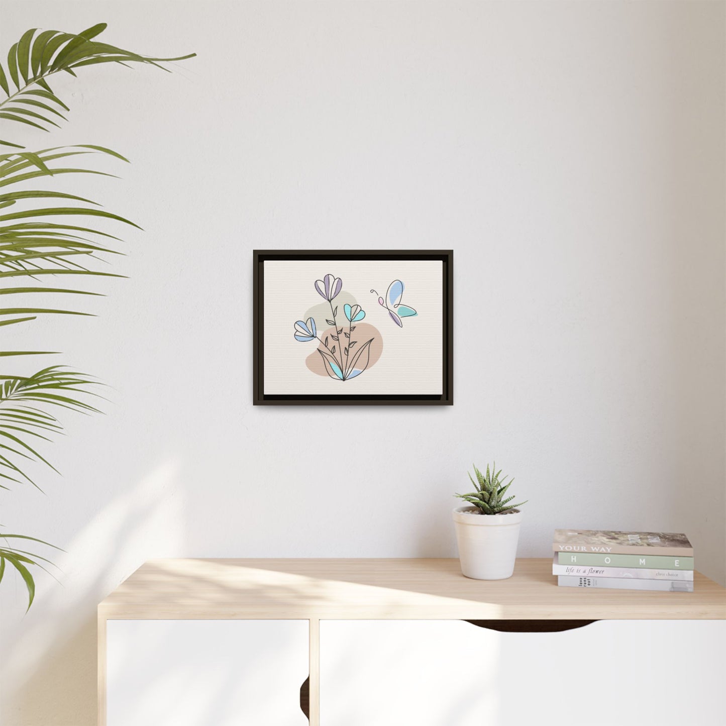 Framed artwork of a dachshund on a wall above a desk with a plant and books.