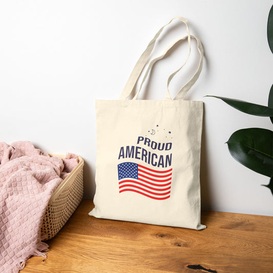 Tote bag with 'Proud American' text and flag design on a wooden surface.